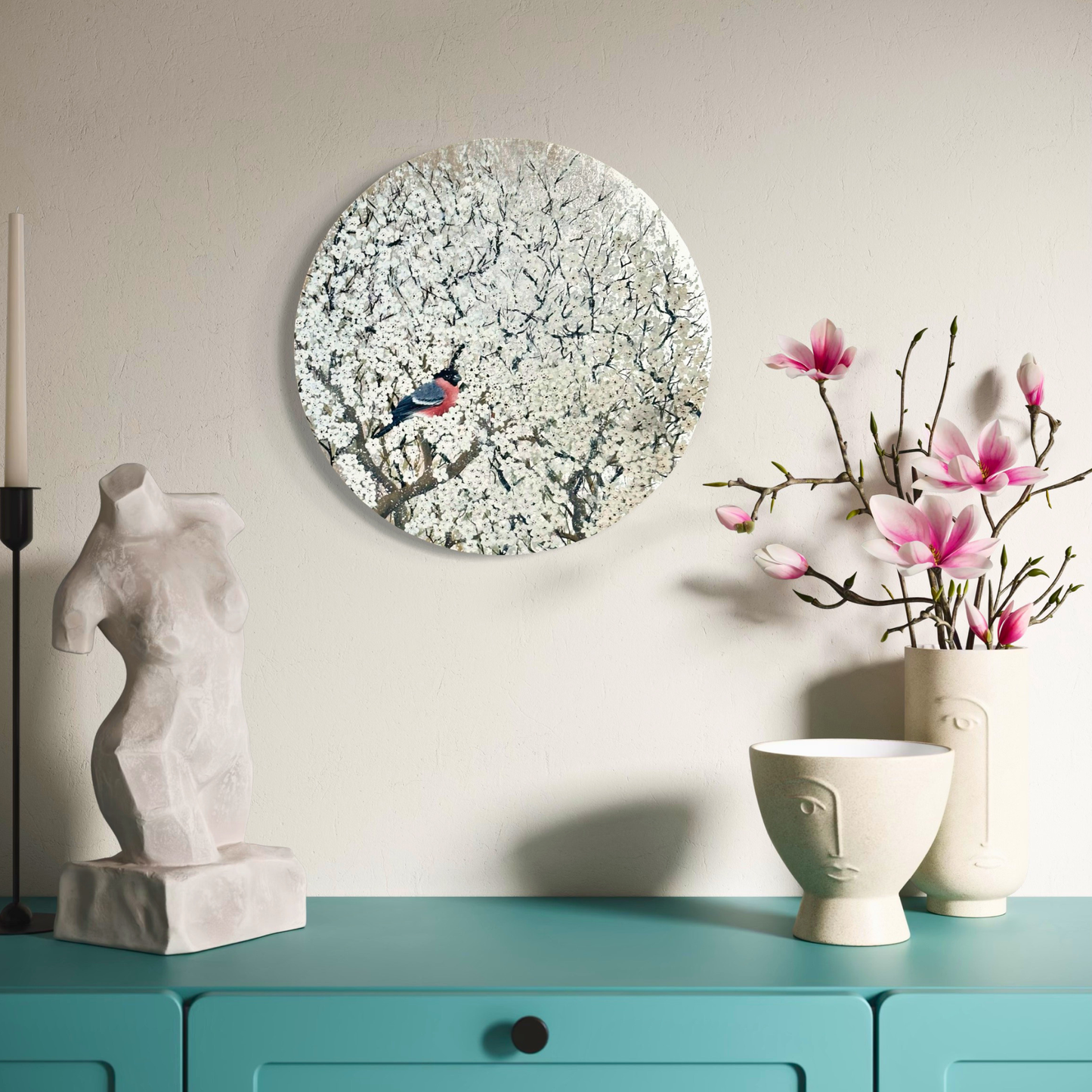 Decorative setup with a round silver blossom painting, sculpture, and floral arrangement on a teal surface.